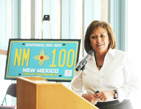 Governor Suzanna Martinez standing at a podium in front of a mockup of a turquoise NM license plate